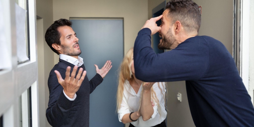 Dois homens brancos e uma mulher branca discutem em um corredor.