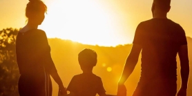 Criança de mãos dadas com seus pais, apreciando o pôr do sol