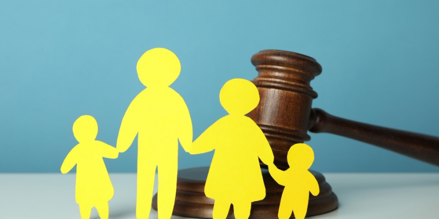 Bonecos de papel simbolizando uma família, dispostos à frente de um martelo do juiz, o qual representa o Sistema Judiciário.